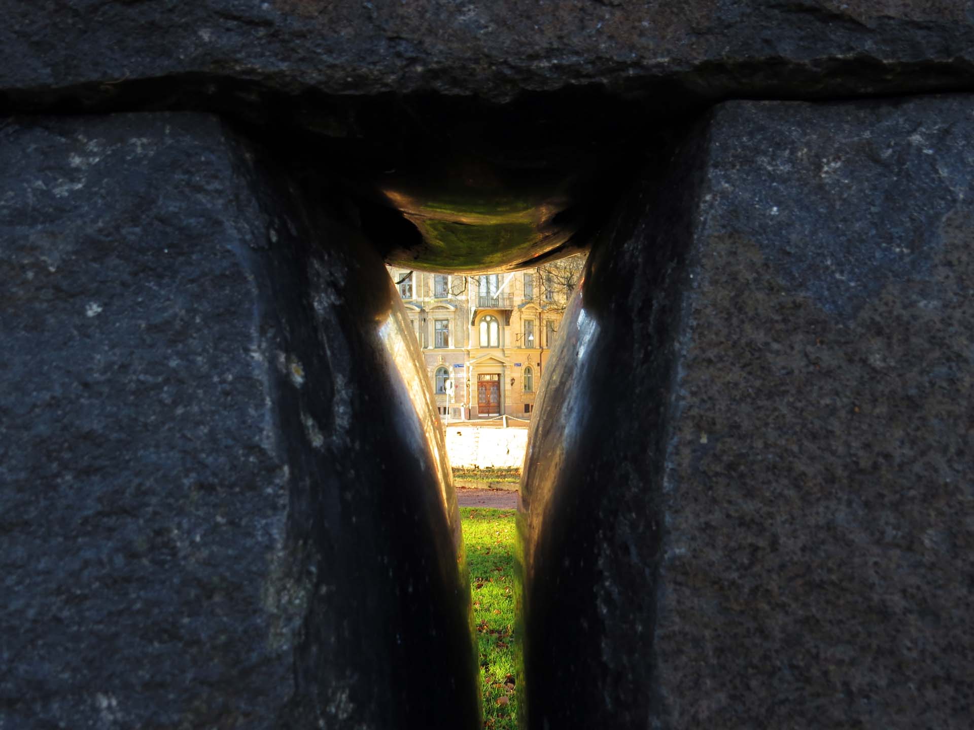 Through the polished thighs of a standing stone sculpture, the door of a building in old central Gothenburg is seen and reflected in the polished stone