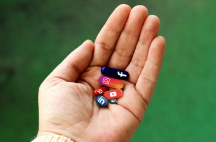 Social Media Addiction. A hand cupping pills, each coloured with a different social media logo. Source credit TodayTesting.com