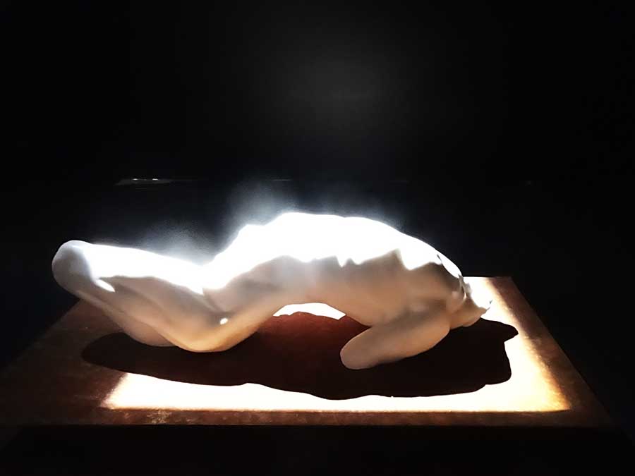 A sculpture of a twisted male torso carved in white marble and illuminated with a strong harsh white spotlight. The photograph is overexposed because of the bright light, such that the light seems to emanate from the figure.