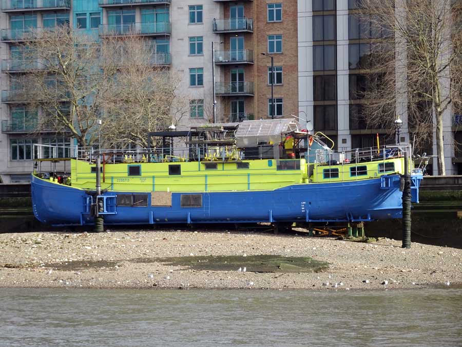 An old boat all made up with new paint but high and dry at low tide, resting on the shingle shore of the Thames opposite the Millbank ferry stop